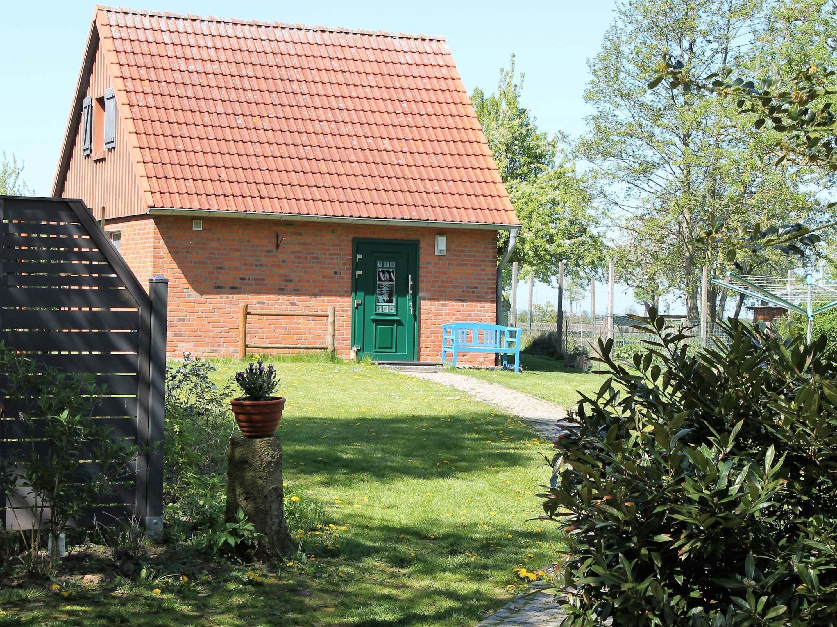 A brick building with a green door, a blue bench, and a garden with a tree stump and potted plant.