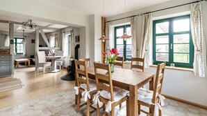 A dining area with a wooden table and chairs, a vase with flowers, and a view of the outside through large windows. - Lovely Holiday Home in Zierow With Terrace (Zierow)