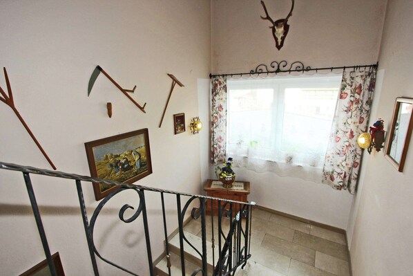 Un escalier avec une rampe en métal, une tête de cerf décorative accrochée au mur et un rideau à motifs floraux devant une fenêtre.