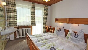 Un dormitorio con cabecera de madera, cama con cubrecama con motivos de bambú, mesita de noche, silla y ventana con cortinas.