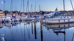 A marina with multiple sailboats docked, surrounded by buildings and a clear sky.