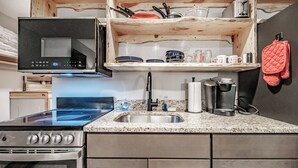 A kitchen with a stove, microwave, sink, and wooden shelves above. - Cascades Studio at Sunday River (Newry)