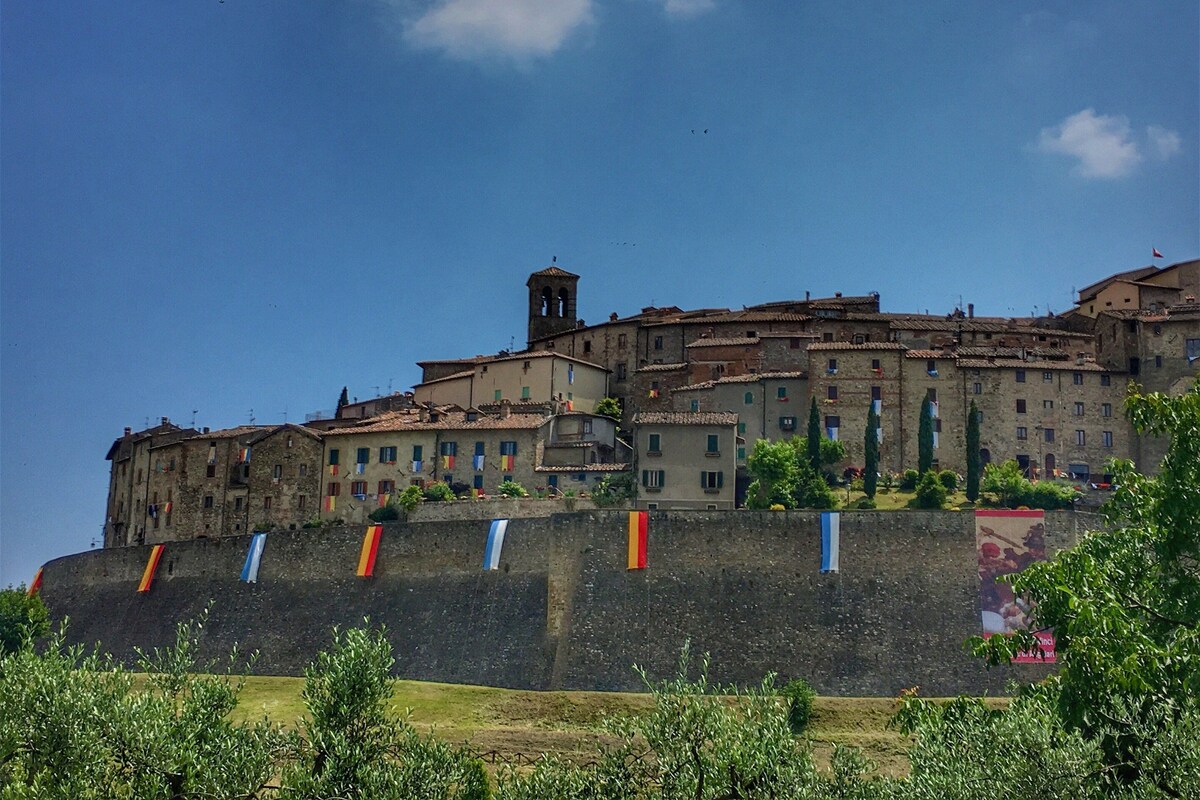 A historic building with multiple levels, a prominent bell tower, and a fortified wall with flags.