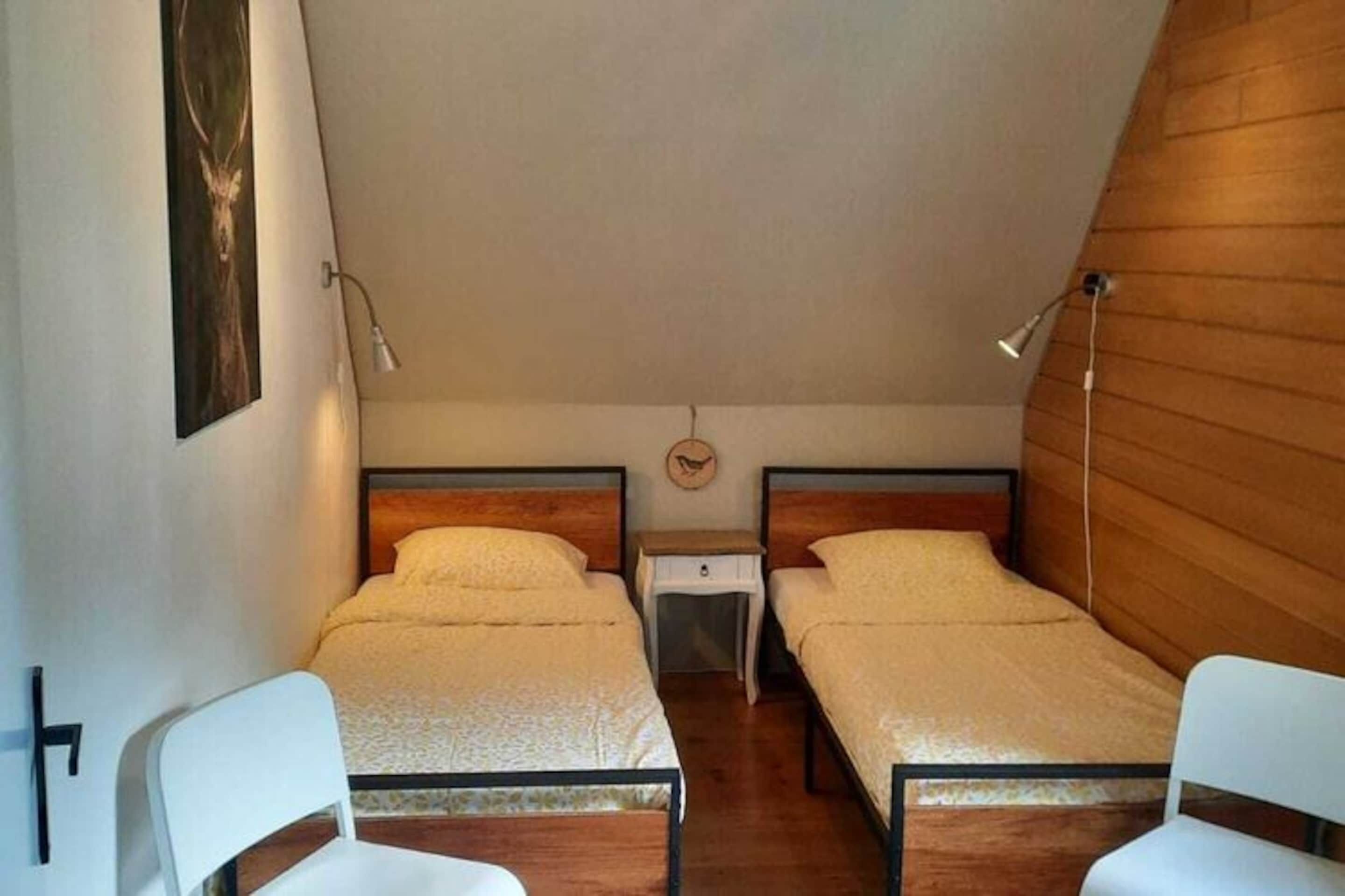 Ein kleines, gemütliches Zimmer mit zwei Einzelbetten, einem Nachttisch und einem Sessel.