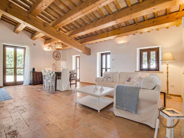 A spacious living area with a high wooden ceiling, a white sofa, a coffee table, and a dining area with chairs and a table. - Stunning Apartment in Mombaroccio Near Metauro River (Mombaroccio)