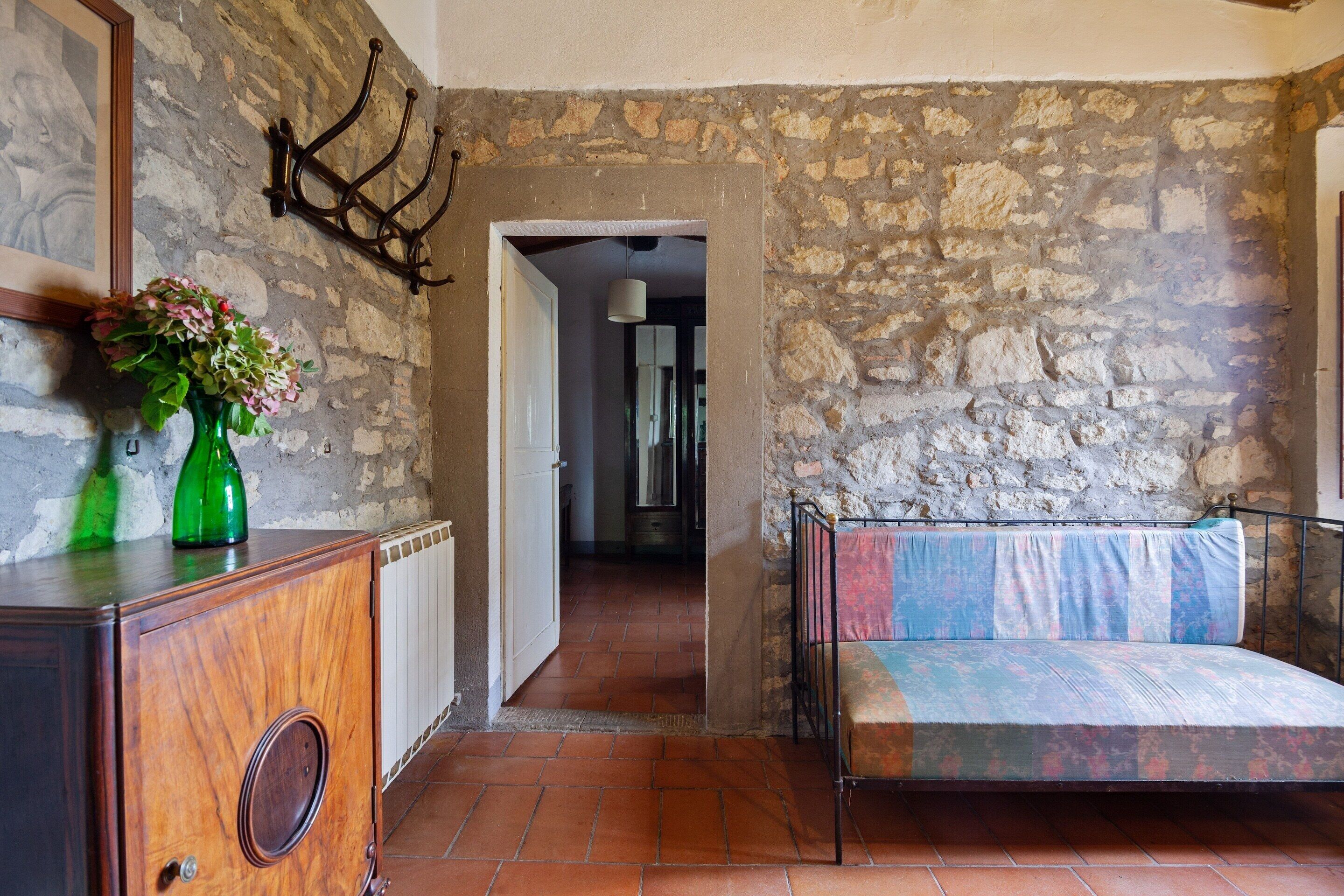 Une pièce avec un mur en pierre, une armoire en bois ornée d’un vase vert et un lit recouvert d’une couvre-lit à motifs.