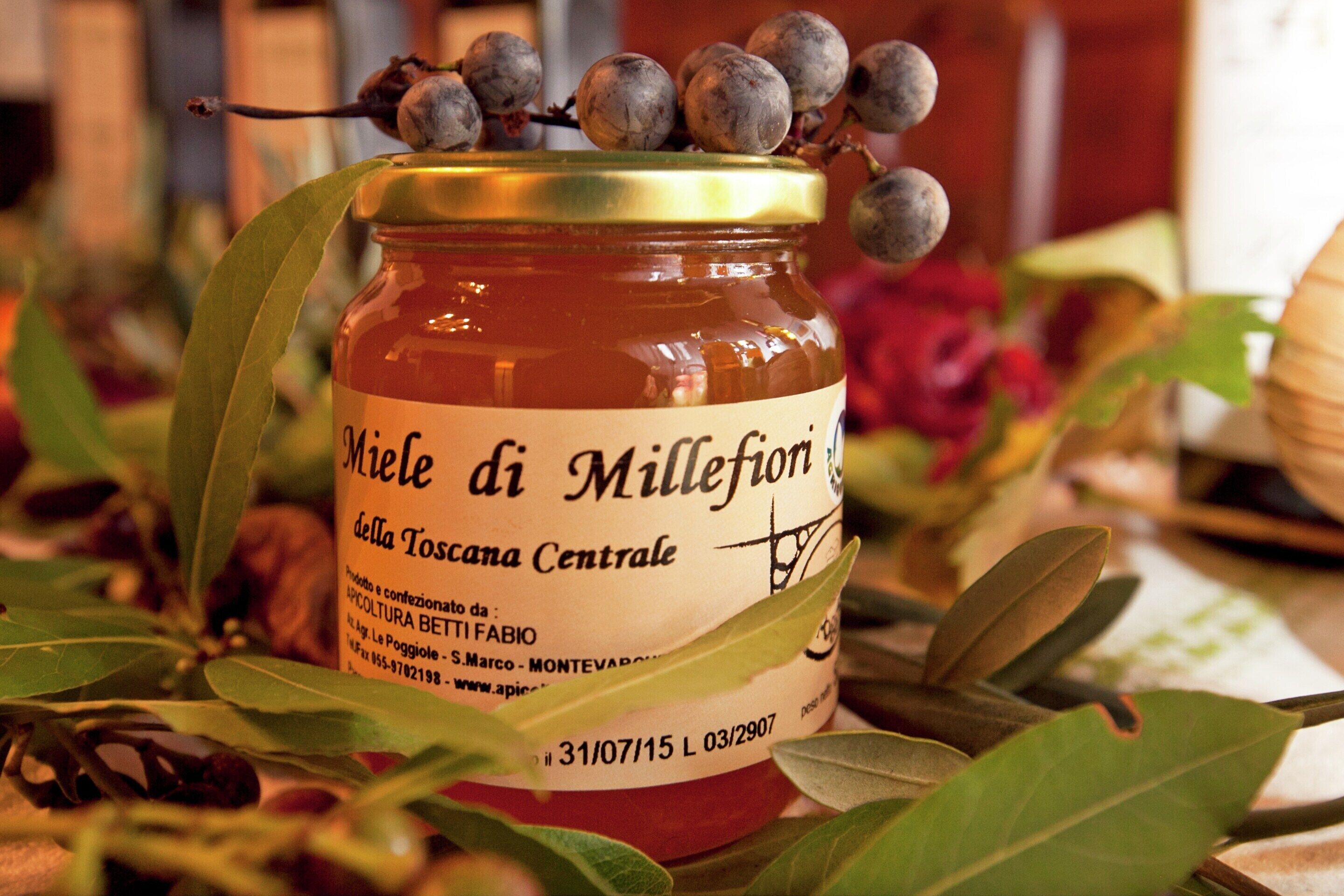 A jar of Miele di Millefiori honey with a label, surrounded by green leaves.