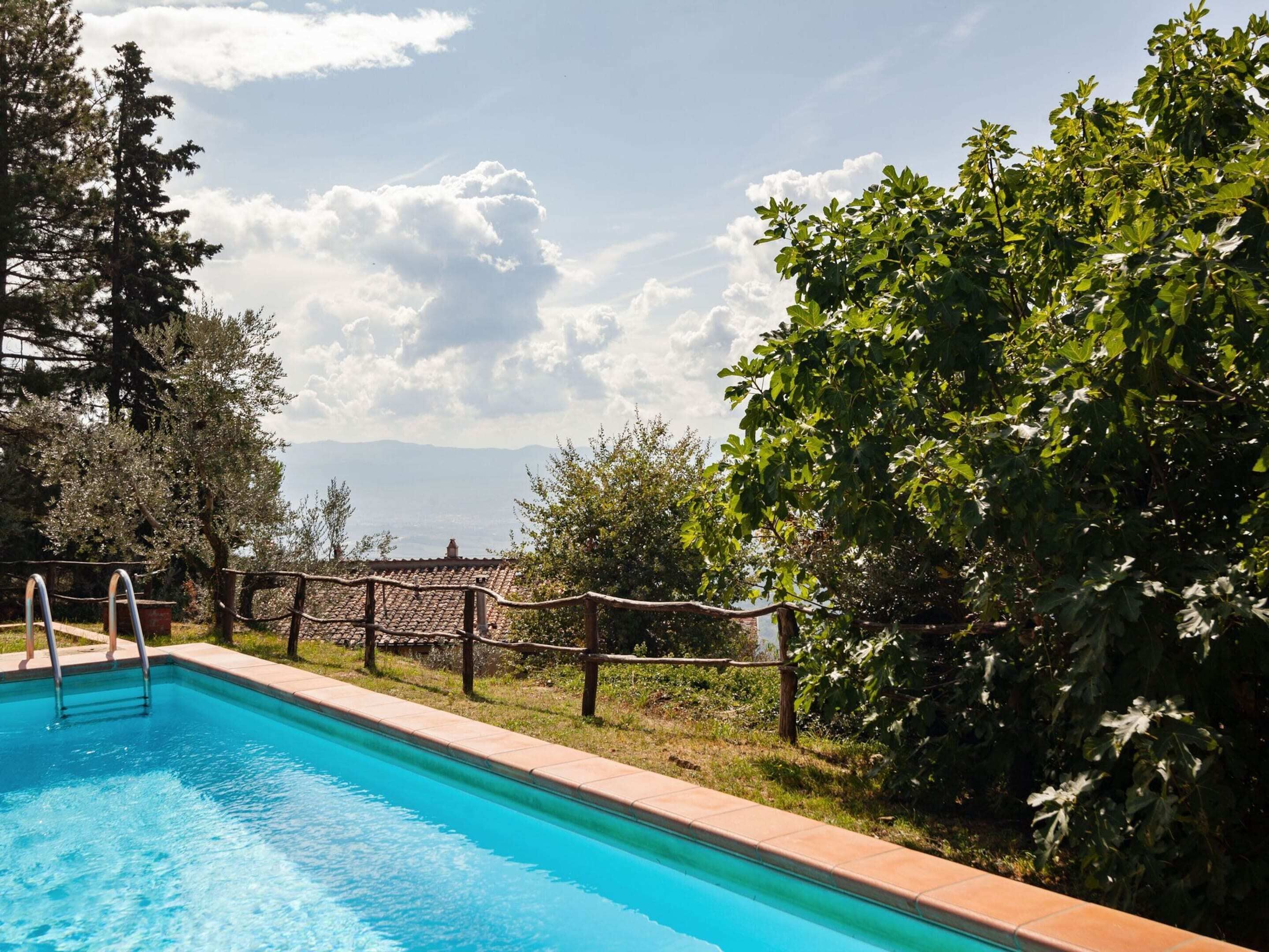 A swimming pool with a wooden fence, surrounded by trees and a view of distant buildings.