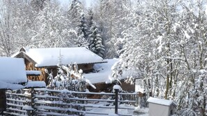 Een met sneeuw bedekte houten chalet met een rustieke uitstraling, omgeven door sneeuwzware bomen en een houten omheining.