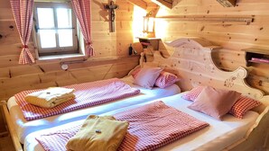 Een houten kamer met twee bedden, geruit beddengoed, een raam met gordijnen en een houten hoofdbord.