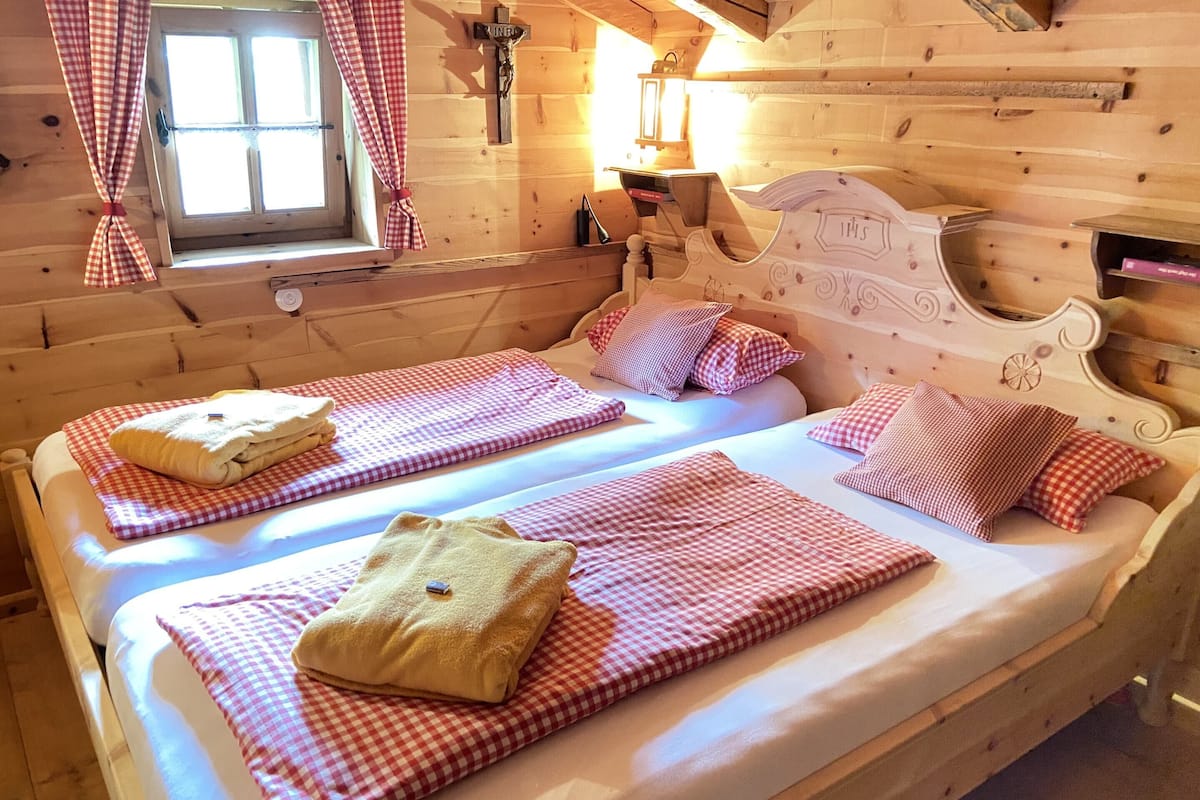 A cozy wooden cabin bedroom with two beds, checkered bedding, and a window with curtains.