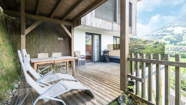 A wooden deck with a table and chairs, a covered seating area, and a view of a mountainous landscape. - Premium Apartments im Zillertal (Hart im Zillertal)