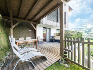 Un patio in legno con tavolo e sedie, una zona salotto coperta e vista su un paesaggio montuoso.