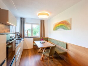 A compact kitchen with modern appliances, a dining area with a bench, and a large window with curtains. - Premium Apartments im Zillertal (Hart im Zillertal)