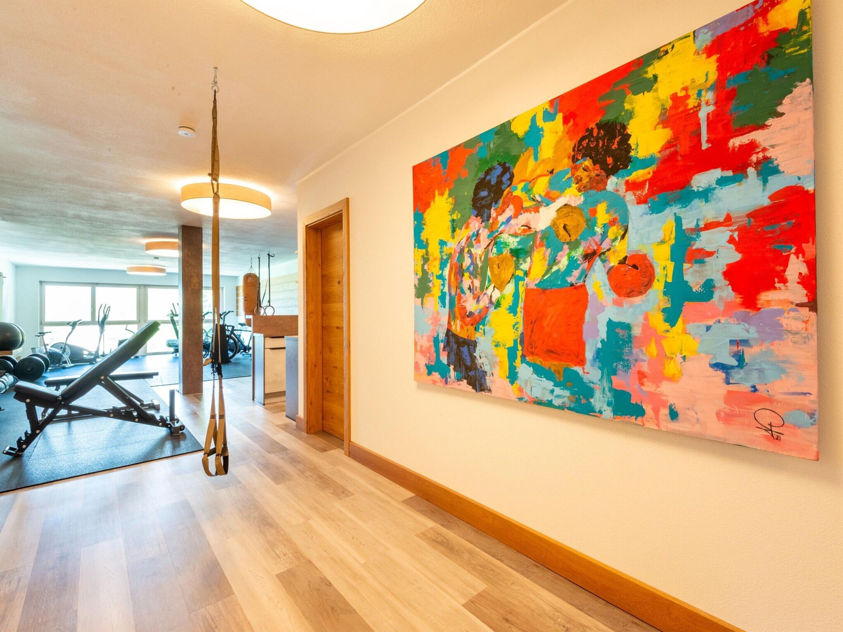 A gym with exercise equipment, a large abstract painting on the wall, and a wooden floor.