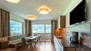 A modern hotel room with a dining area, a kitchen with a flat-screen TV, and large windows offering a scenic view. - Premium Apartments im Zillertal (Hart im Zillertal)