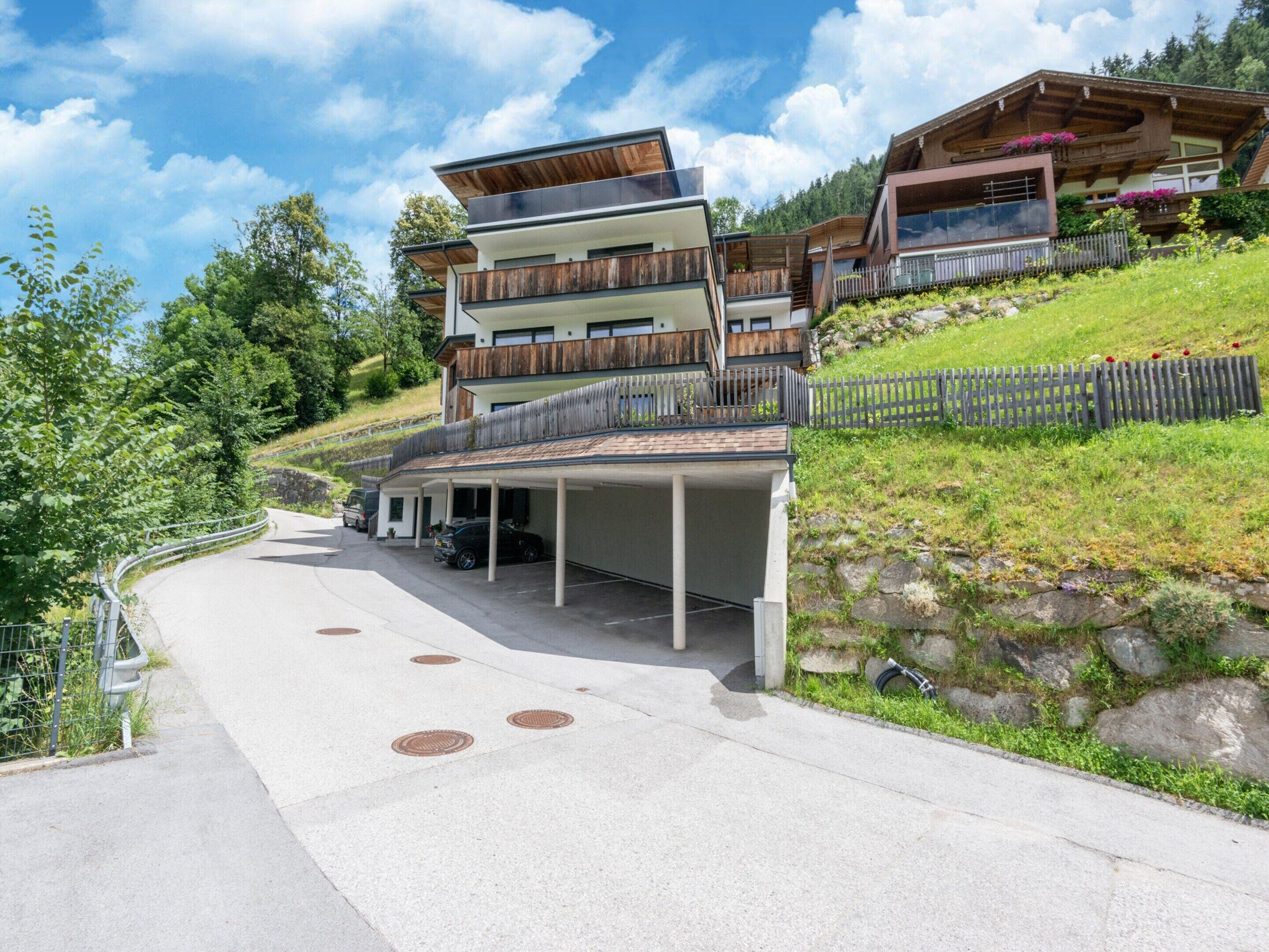Un immeuble moderne à plusieurs étages, doté d’un parking couvert et d’une allée en pente.