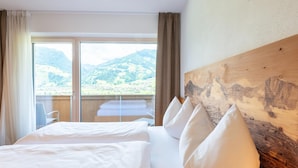 A hotel room with a large bed, a wooden headboard, and a view of mountains through a large window. - Premium Apartments im Zillertal (Hart im Zillertal)
