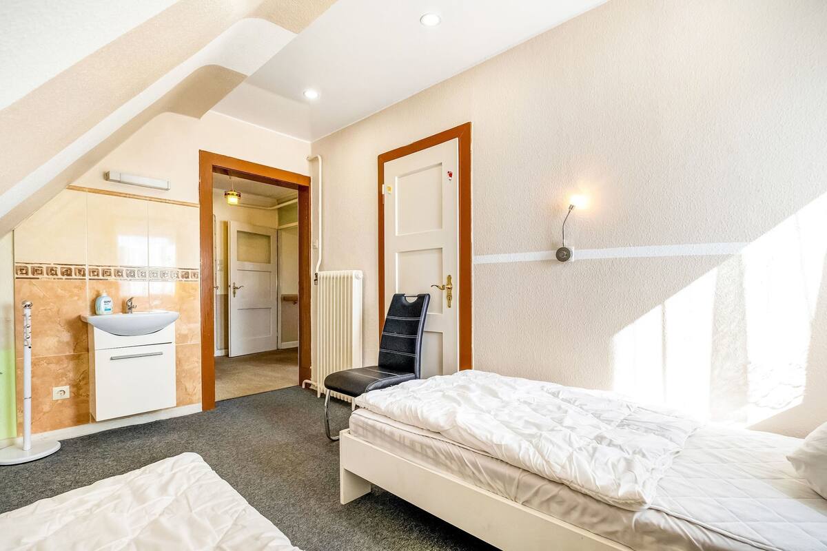 A bedroom with a bed, a chair, a sink, and a radiator.