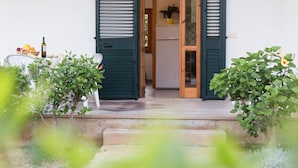 A house entrance with open shutters, a table with fruits and a bottle, and two potted plants. - Nice Residence in San Nicolo di Ricadi With Pool (Ricadi)