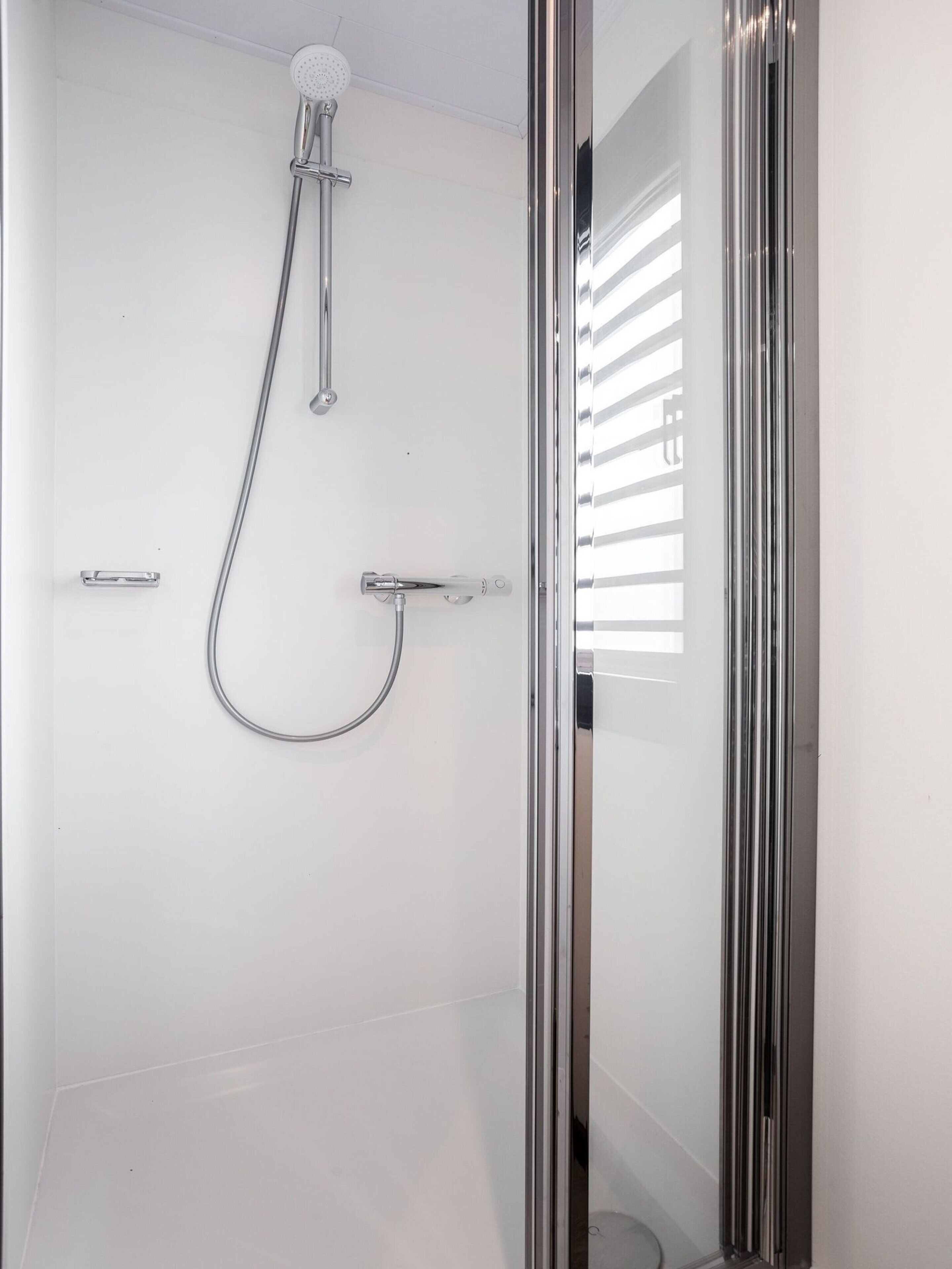 A modern shower with a glass door, chrome fixtures, and a ceiling-mounted showerhead.