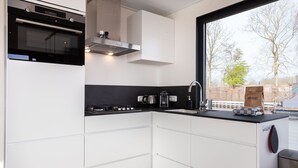 A modern kitchen with white cabinetry, a black countertop, and a window providing a view of the outside. - Unique Houseboat on and Around the Sneekermeer (Offingawier)
