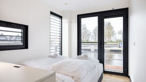 A modern hotel room with two beds, a desk, and a large window overlooking a body of water. - Unique Houseboat on and Around the Sneekermeer (Offingawier)