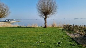 A grassy area with a tree and a dock extending into a calm lake. - Unique Houseboat on and Around the Sneekermeer (Offingawier)