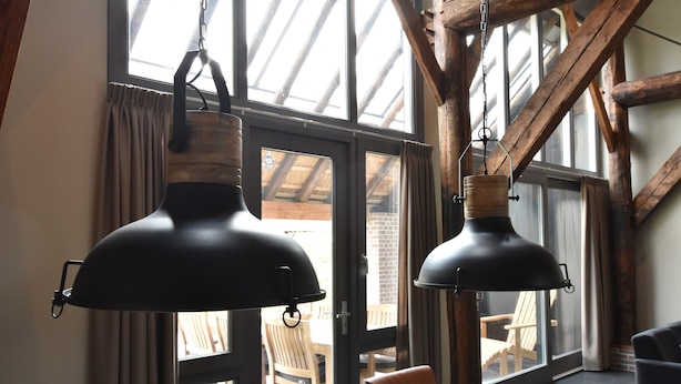 Un comedor con una mesa y sillas de madera, ventanas grandes con cortinas y lámparas colgantes negras.