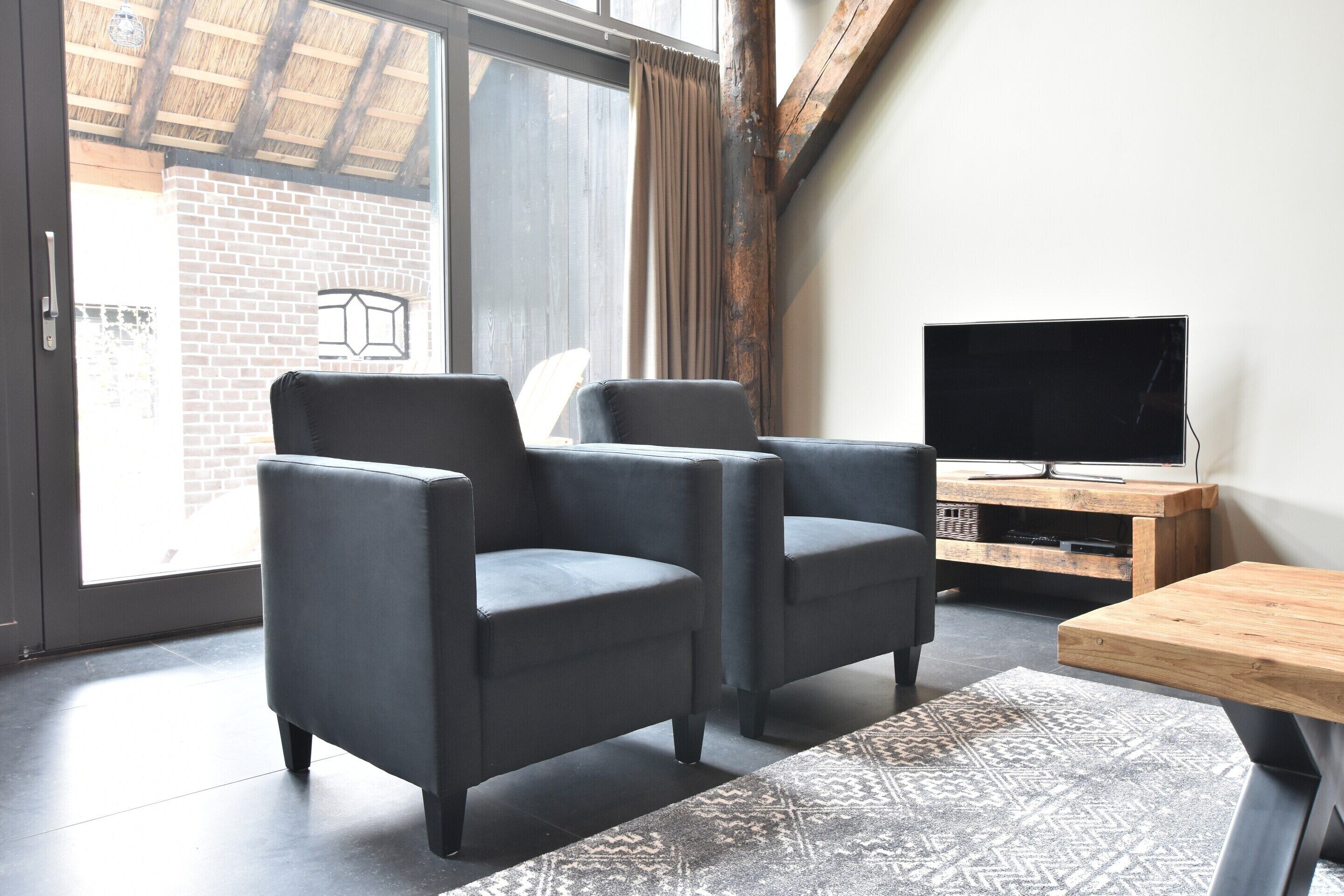 Un salon moderne avec deux fauteuils sombres, une table basse en bois et un téléviseur posé sur un meuble en bois.