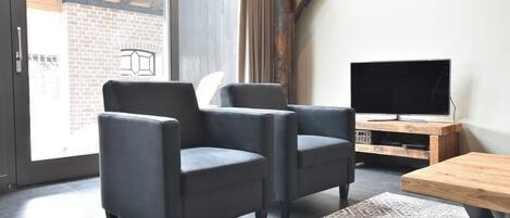 Un salon moderne avec deux fauteuils sombres, une table basse en bois et un téléviseur posé sur un meuble en bois.