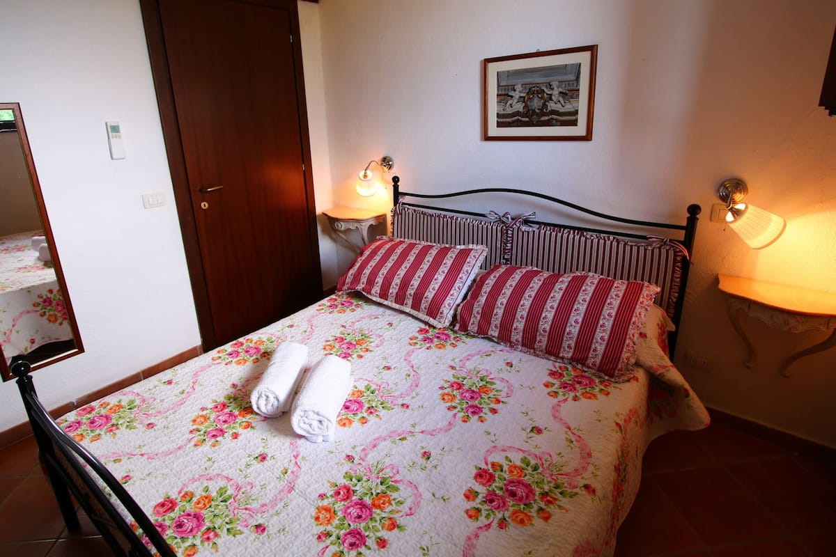 Un lit bien fait, avec une literie à motifs floraux et des oreillers à rayures, une porte en bois, un tableau accroché au mur et des lampes de chevet.