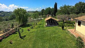 Paesaggio rurale con una piccola casa circondata da un prato curato e alberi.