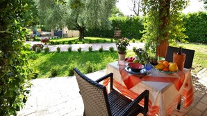 Area pranzo all'aperto con un tavolo apparecchiato per due, immersa nel verde e con vista su un giardino.