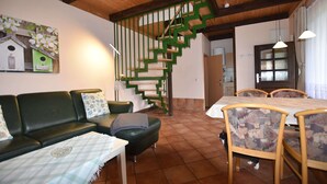 A living room with a green staircase, a dining table with chairs, a sofa, and a cat. - Ferienhaus in der Naehe der Ostsee (Neubukow)