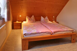 A bedroom with a wooden ceiling, a bed with floral bedding, two bedside lamps, and a nightstand. - Ferienhaus in der Naehe der Ostsee (Neubukow)