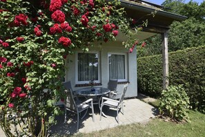 A patio with a table and chairs, surrounded by a garden with red roses. - Ferienhaus in der Naehe der Ostsee (Neubukow)