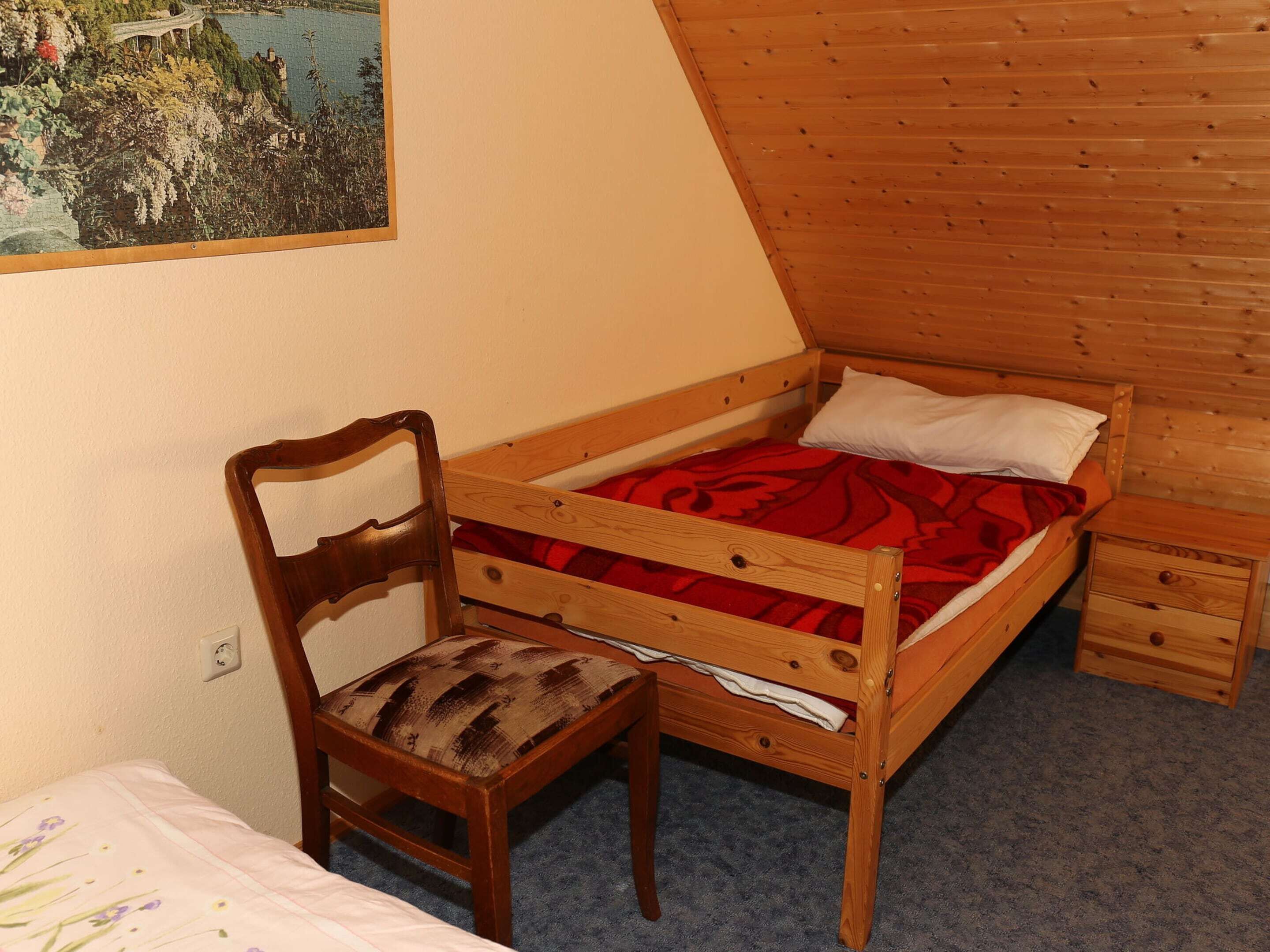 A small, single-room cabin with a wooden bed, a chair, and a small table.