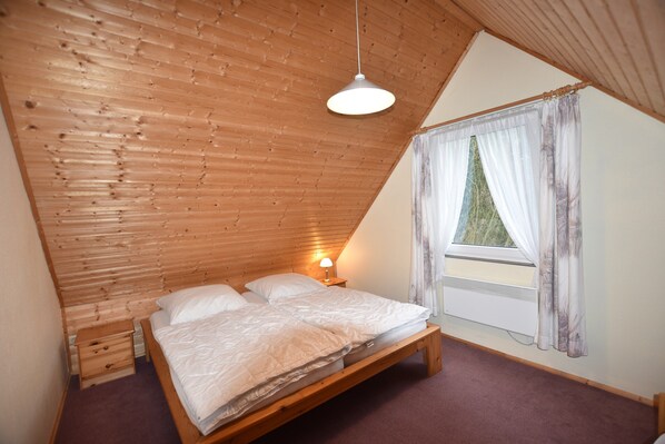 Ein Schlafzimmer mit Holzboden, einem Einzelbett, einem Nachttisch, einem Fenster mit Vorhängen und einem Wandheizkörper.