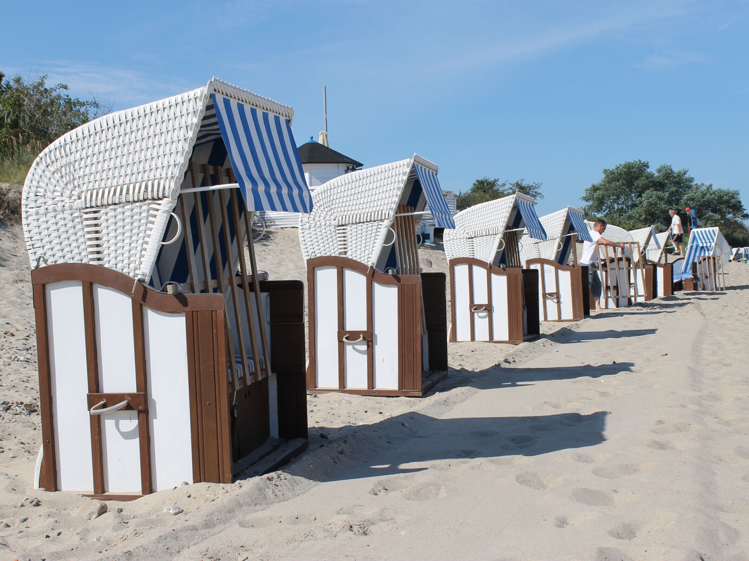 Beach huts with striped awnings, arranged in a row on a sandy beach.