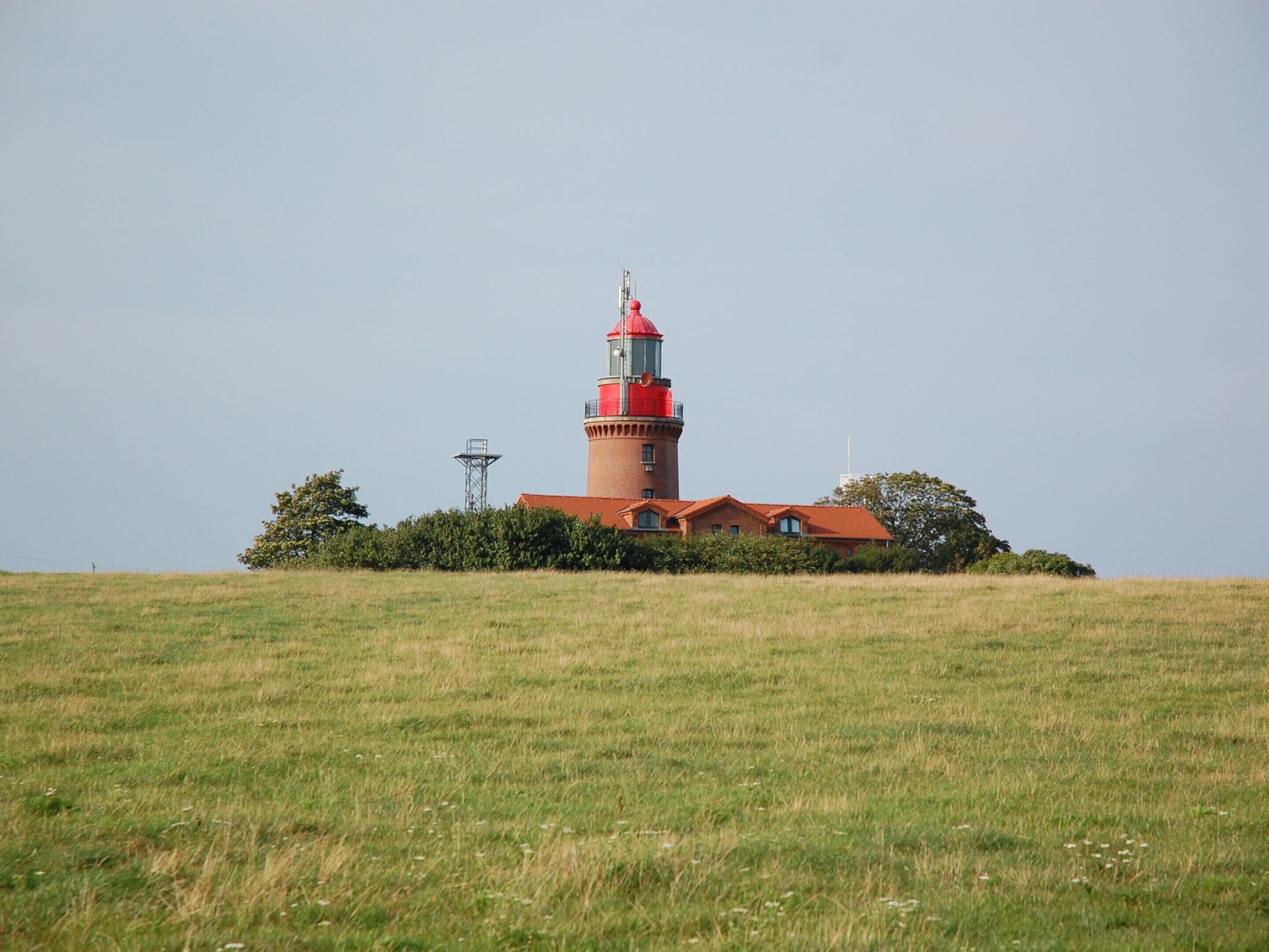 Een vuurtoren met een rode bovenkant en een bakstenen basis, omgeven door een grasveld en enkele bomen.