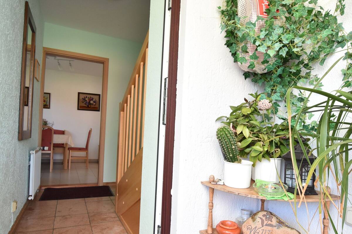 Un couloir avec une porte en bois, une chaise, une table et une petite étagère sur laquelle se trouvent un cactus et une pancarte de bienvenue.