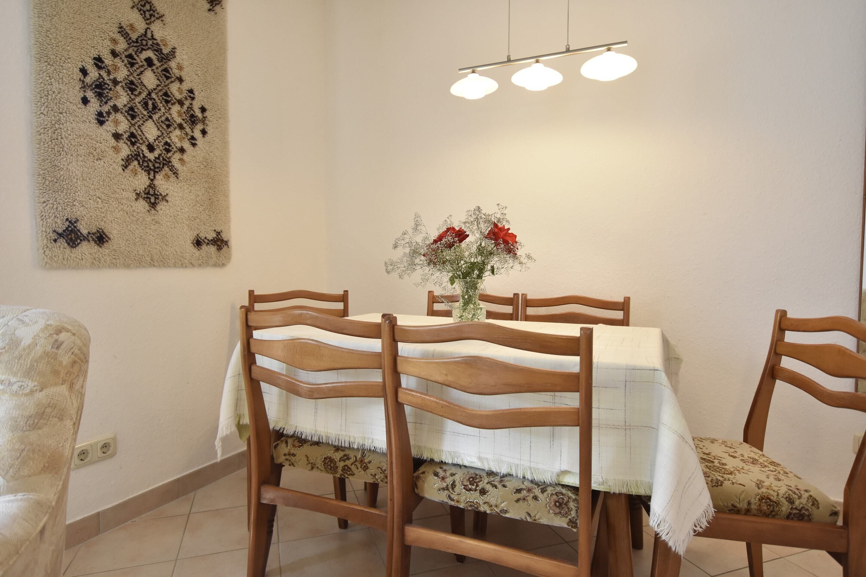 Comedor con una mesa dispuesta para cuatro, sillas de madera, un florero con flores y una lámpara colgante.