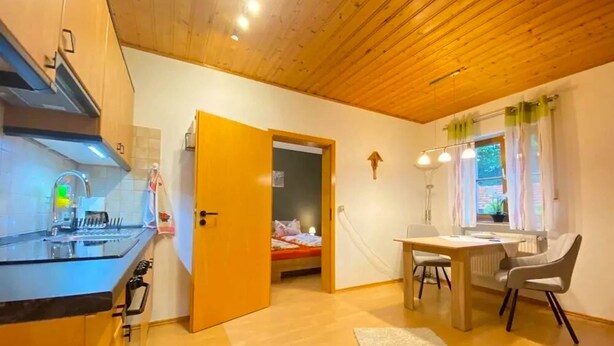 A compact kitchen with modern appliances, a dining area with a table and chairs, and a bedroom with a bed. - Comfortable Apartment in Zenting in Lower Bavaria (Zenting)