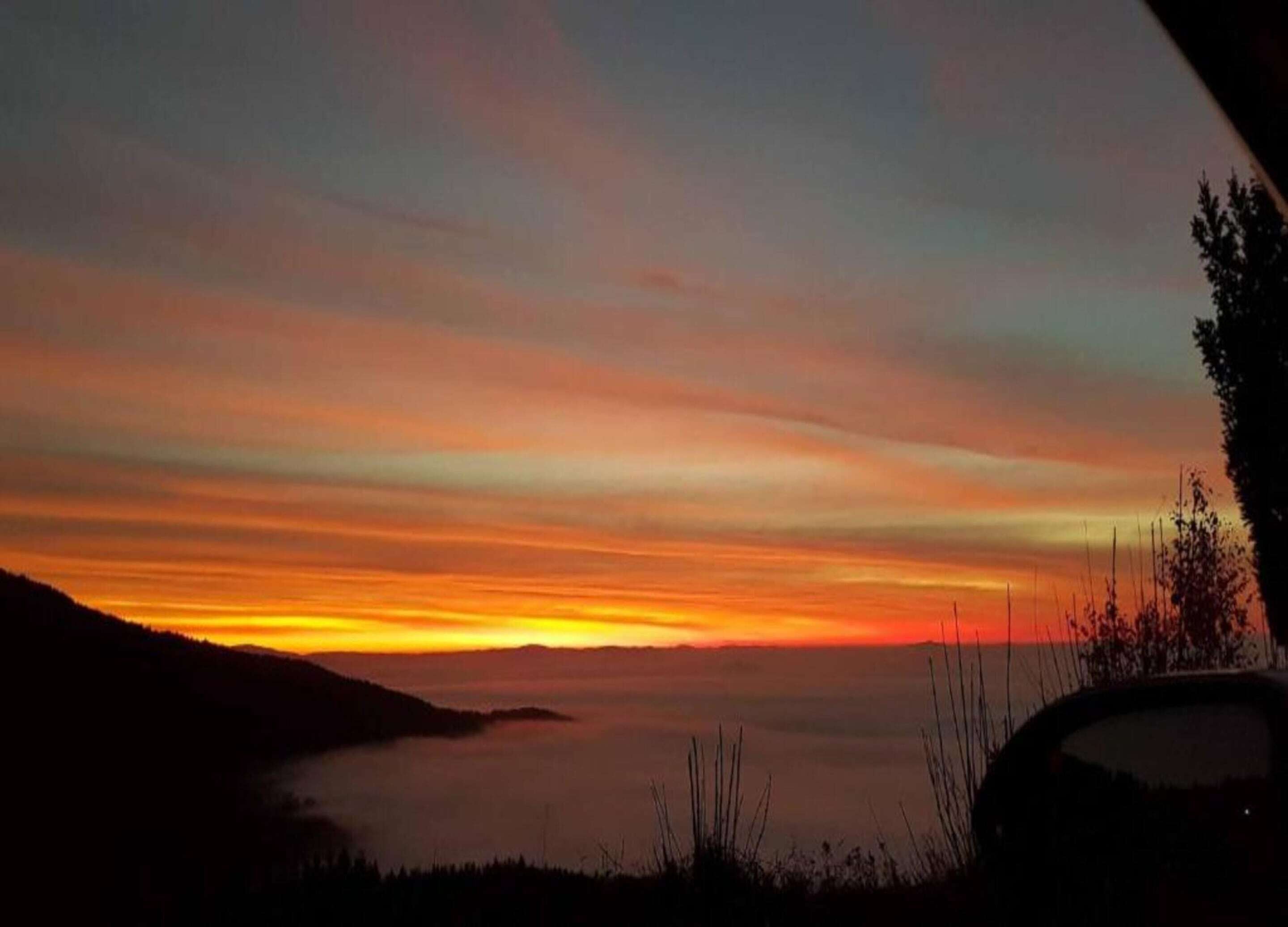 Un coucher de soleil sur une étendue d’eau, avec la silhouette d’une voiture et de la végétation au premier plan.