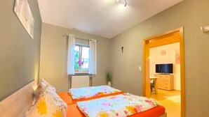 A bedroom with two beds, a window with curtains, a cross on the wall, and a TV in the adjacent room. - Comfortable Apartment in Zenting in Lower Bavaria (Zenting)