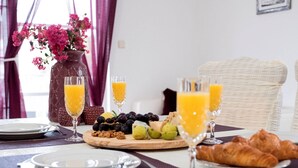 En morgenmadsopstilling med et bord dækket til to, med croissanter, et fad med frugt og to glas appelsinjuice.