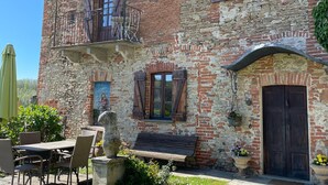Ein rustikales Steinhaus mit Balkon, Holztür und Außenbestuhlung.