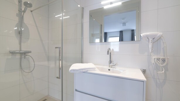 A modern bathroom with a glass shower enclosure, a white sink with a mirror above it, and a hairdryer mounted on the wall. - Luxury 8-person Wellness Villa With Sauna and Outdoor hot tub is Unique (Colijnsplaat)