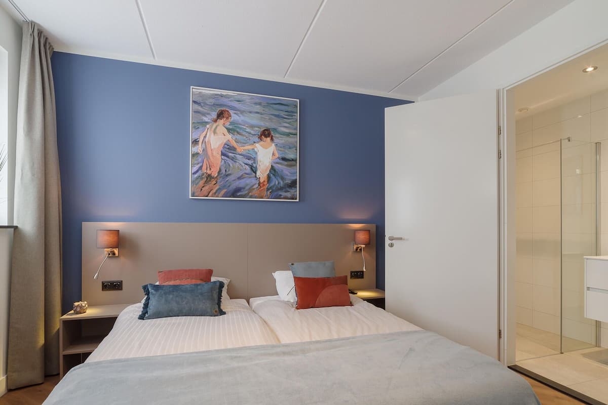 Ein Hotelzimmer mit einem großen Bett, zwei Nachttischen mit Lampen, einem Bild an der Wand und einer Duschabtür aus Glas.